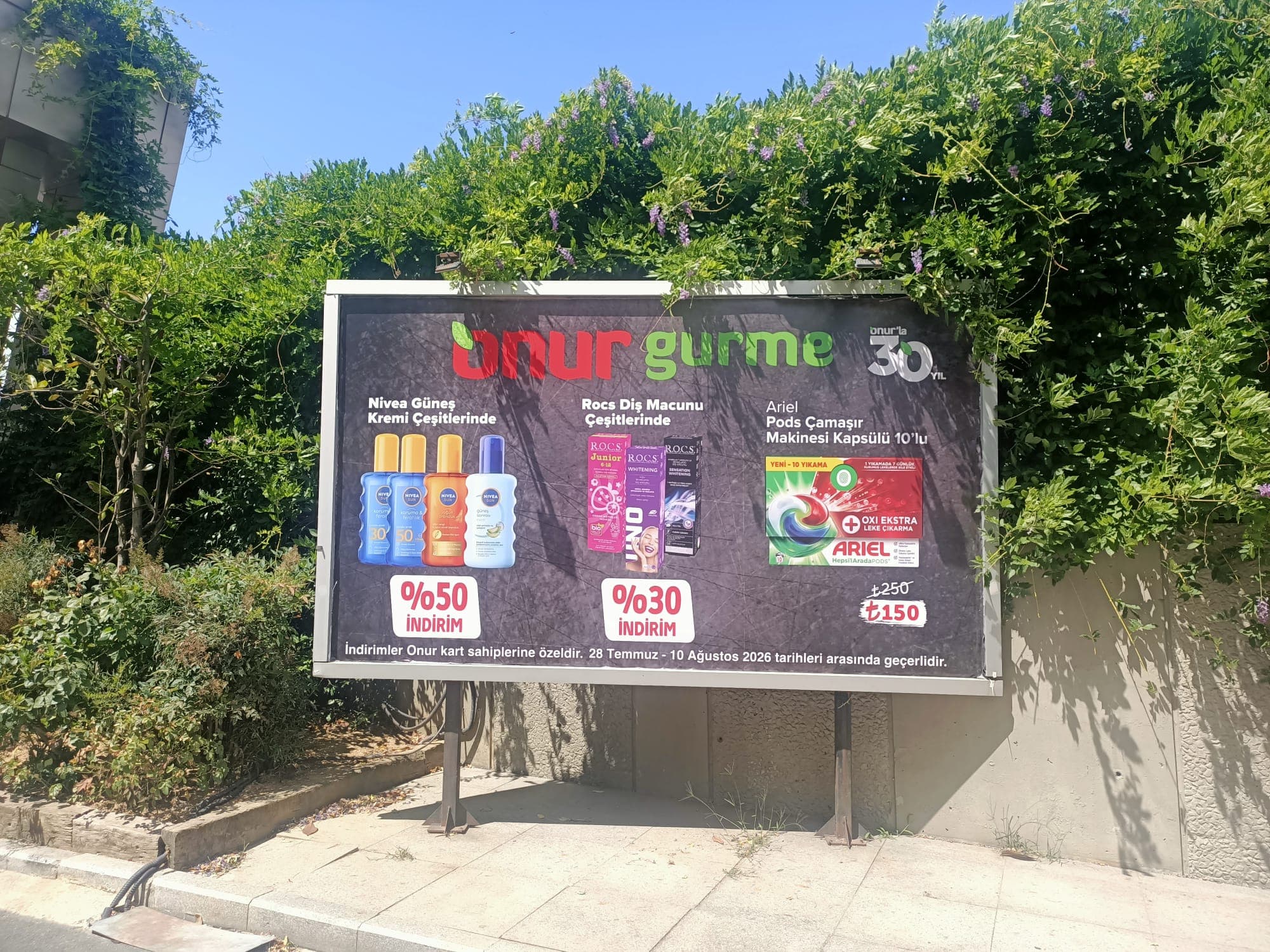 Üzerinde indirimli market ürünleri ve yüzde elli ile yüzde otuz indirim ibareleri olan yol kenarı bilboardı