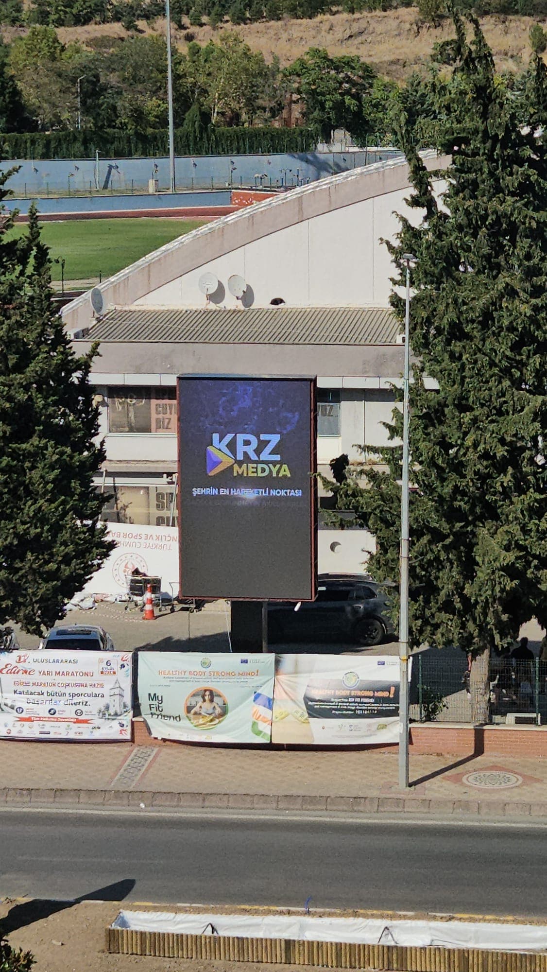 Cadde kenarında KRZ Medya içeriği yayınlayan LED totem, altında belediye brandaları