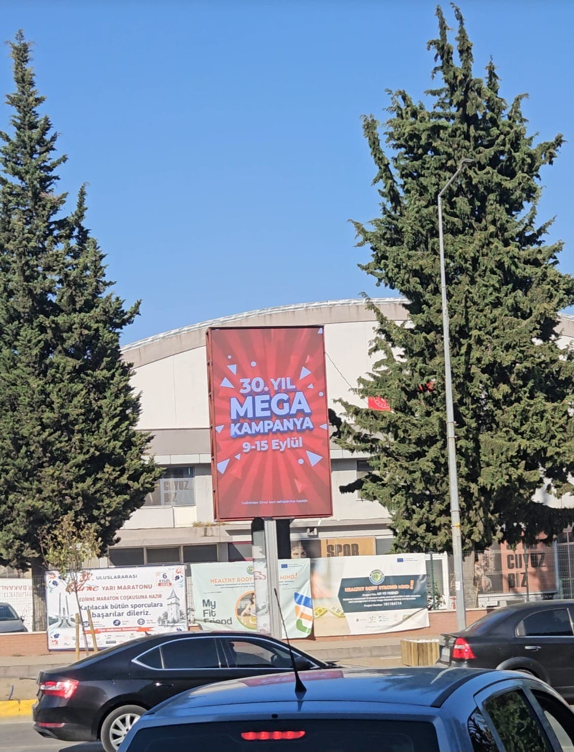 Kırmızı zeminde kampanya duyurusu yayınlayan LED totemin cadde karşısından görünümü